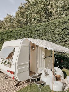 an old camper is parked in the grass with its door open and some chairs around it