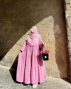 a woman in a pink dress is standing near a stone wall and holding a flower pot