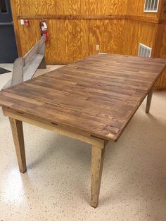 a large wooden table sitting on top of a white tile floor next to a wood paneled wall