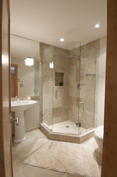 a bathroom with a walk in shower next to a white toilet and sink on a rug