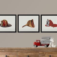 three framed pictures on the wall above a dresser with a teddy bear and fireman's hat