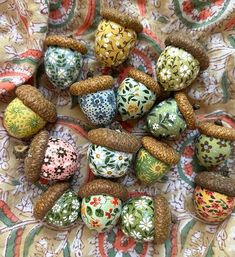 many different colored eggs are sitting on a table cloth with pine cones in the middle