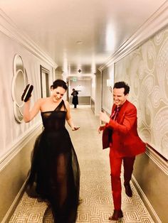 a man in a red suit and woman in a black dress walking down a hallway