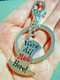 a hand holding a metal keychain that says, we're all mad here