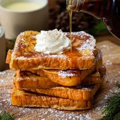 a stack of french toast topped with whipped cream and syrup being drizzled over it