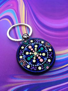 a round keychain with colorful designs on it sitting on a purple background that is swirling