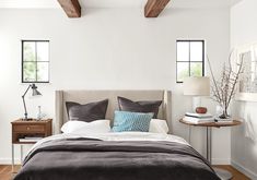 a bed with pillows and blankets in a bedroom next to a table with two lamps on it