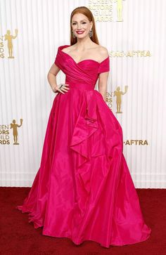 a woman in a pink dress standing on a red carpet with her hands on her hips