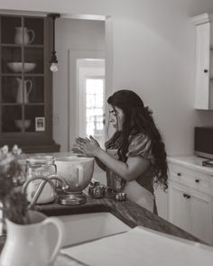 a woman standing in a kitchen next to a counter filled with bowls and pans