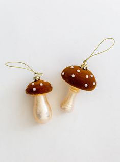 two brown mushrooms with white dots hanging from gold - plated earwires on a white background