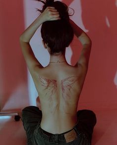 a woman sitting on the floor with her back turned to the camera and tattoos on her chest