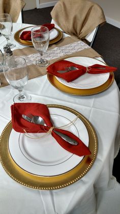 the table is set with red napkins and gold place settings for two people to eat