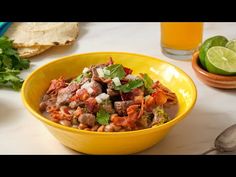 a yellow bowl filled with meat and vegetables next to some tortilla chips on a table