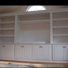 an empty living room with white bookcases and a blue couch in front of the window