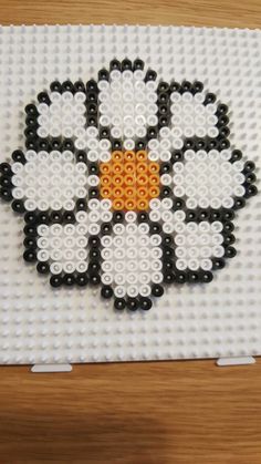 a flower made out of legos sitting on top of a wooden table with white and black beads