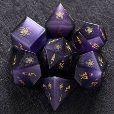 purple and gold dice set with spider symbols on them, sitting on a black surface