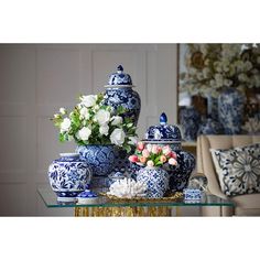 blue and white vases with flowers in them on a glass table next to a couch