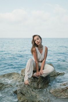 a woman sitting on top of a rock next to the ocean with her eyes closed