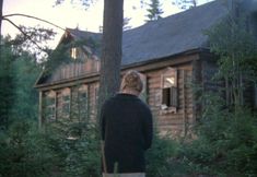 a woman standing in front of a log cabin looking out at the woods and trees