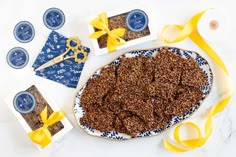 a table topped with blue and white plates filled with granola next to scissors and yellow ribbons