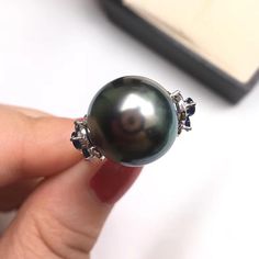 This is a stylish and beautiful ring earring. Product Information Origin Tahitian Pearl Jewelry Processed in Japan Material Tahitian Pearl and 18K White Gold Dimensions Custom Pearl Shaped: Round Size: 14-15mm Black Tahitian Pearl Quality: AAAA Nacre: Very Thick Color: Black with Peacock Green Luster Luster: Very High Accessories Metal: 18K White Gold Other: 0.60ct of SI Quality Natural Diamond and 1.80ct of Sapphire Luxury Tahitian Pearl Jewelry For Anniversary, Luxury Tahitian Pearl Anniversary Jewelry, Tahitian Pearl Gemstone Jewelry, Round Tahitian Pearl Gemstone Jewelry, White Gold Tahitian Pearl Jewelry With High Luster, Tahitian Pearl Jewelry With High Luster, Round Tahitian Pearl Jewelry With High Luster, Tahitian Pearl Jewelry For Anniversary, Fine Jewelry Black Pearl Ring