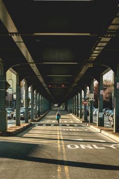 a person is walking down the street under an overpass with cars parked on both sides