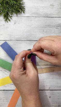 someone cutting out strips of colored paper with scissors on a white wooden table next to a plant