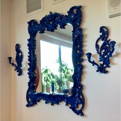 an ornate blue mirror hanging on the wall next to a window with potted plants