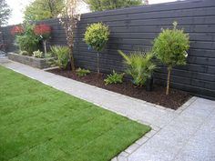 a black fenced in area with green grass and plants on the side walk way