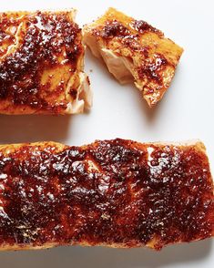 two pieces of meat with sauce on them sitting on a white surface next to another piece of bread