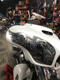 a white and black motorcycle parked inside of a garage next to a man in a blue shirt