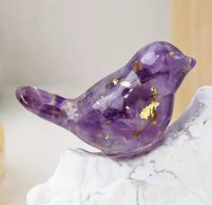 a purple glass bird sitting on top of a white piece of rock with gold flecks