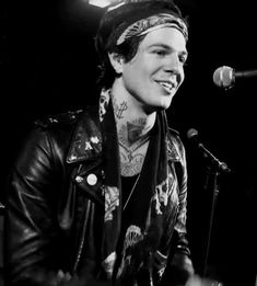 a black and white photo of a man with tattoos on his face singing into a microphone