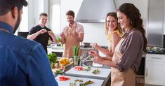 a group of people standing around a kitchen preparing food on top of a white counter