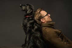 a man sitting with his dog in front of him on a black background wearing glasses