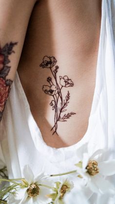 a woman's back with tattoos on her body and flowers in the foreground