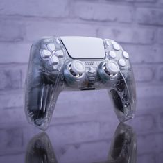 a video game controller sitting on top of a glass table next to a brick wall