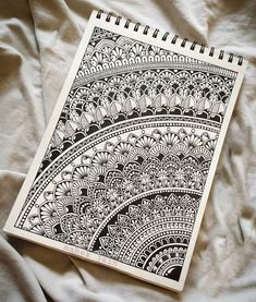 a notebook and pen sitting on top of a white sheet covered in black ink with intricate designs