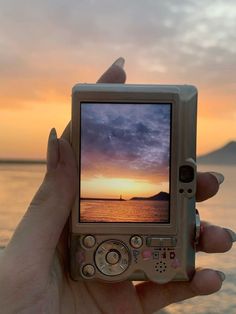 a person holding up a small device in front of the ocean at sunset or sunrise