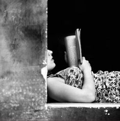 a woman laying on the ground reading a book while holding an open book in her hand