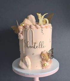 there is a pink cake with gold decorations on the top and butterflies on the side