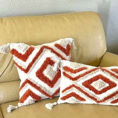 two red and white pillows sitting on top of a tan leather couch next to each other