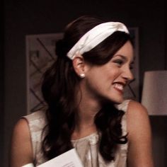 a woman in a white dress is smiling and holding some papers while wearing a headband