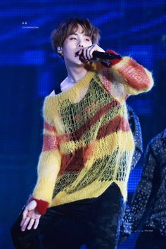 a male in a yellow and red sweater is holding a microphone up to his ear