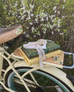 two books tied to the back of a white bicycle with flowers in the background,