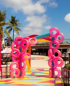 an outdoor playground with pink and blue rings on it's sides, surrounded by palm trees