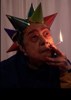 an old woman wearing party hats and holding a lit candle