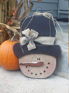 a wooden snowman with a hat and bow on it's head next to pumpkins