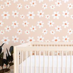 a white crib in front of a pink wall with flowers on it and a potted plant next to the crib