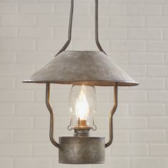 an old fashioned light hanging from a ceiling fixture with a brick wall in the background